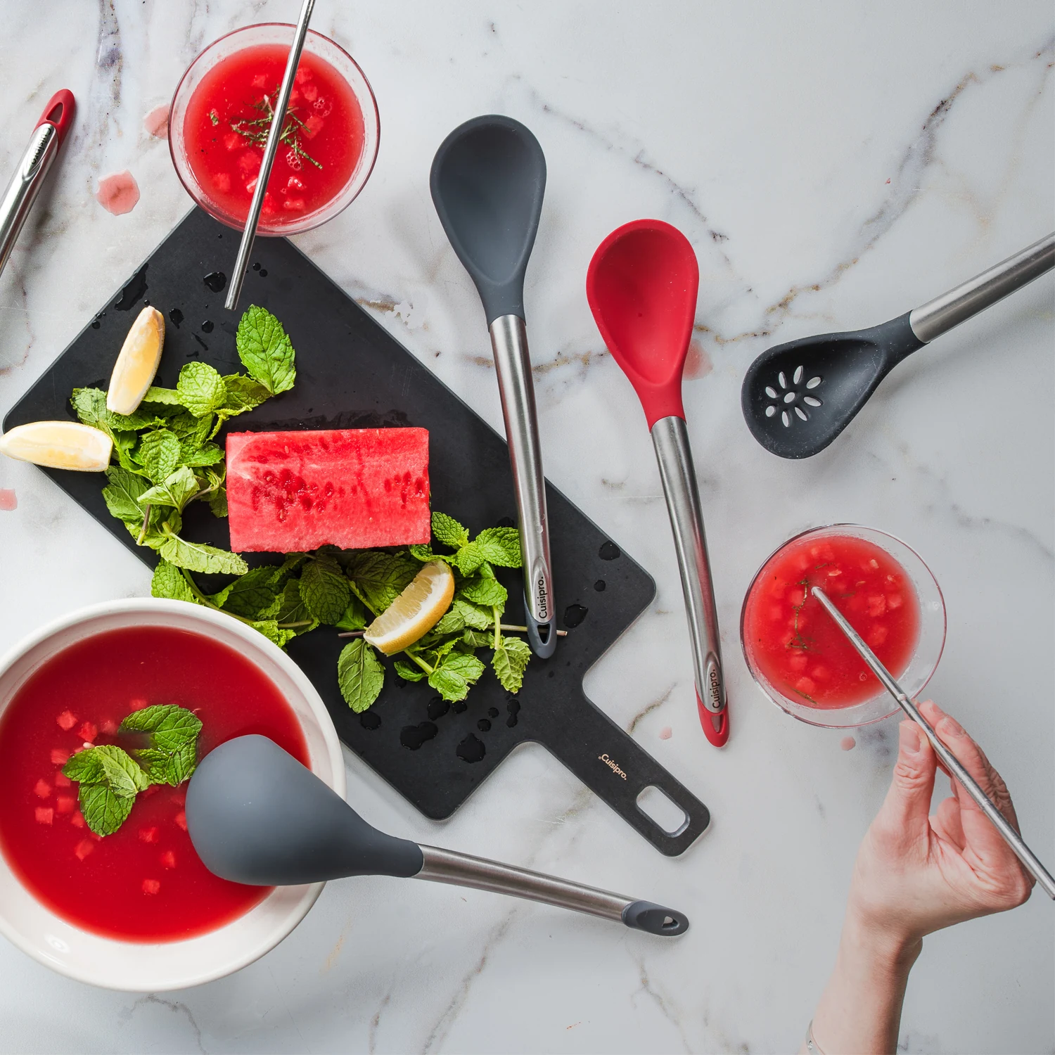 Cuisipro-Küchenhelfer mit roten und grauen Silikonköpfen neben Wassermelone und Minze